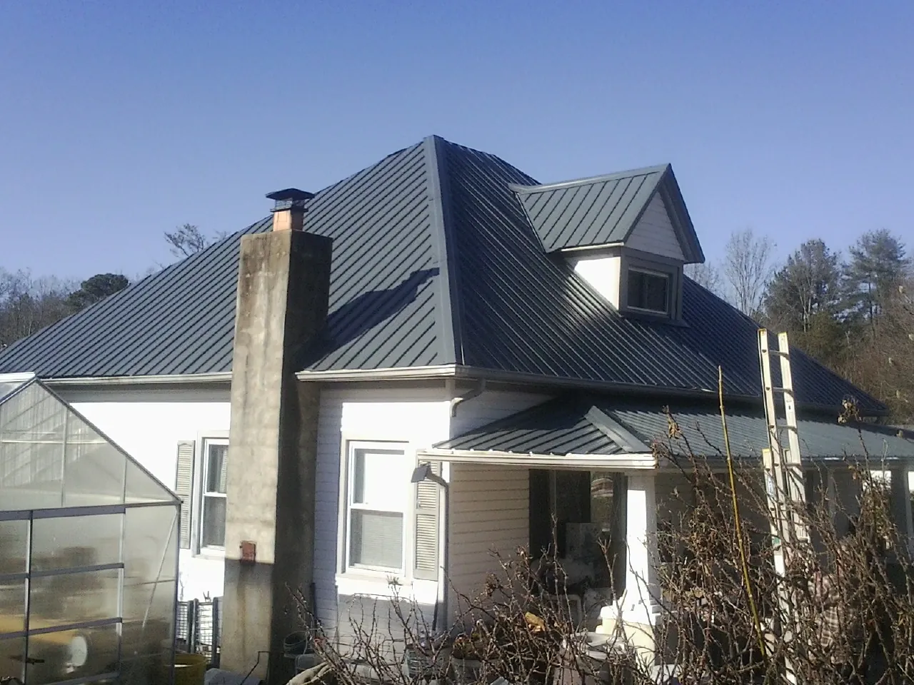 Dark blue standing seam metal roof on a white farmhouse with dormer — Slate & Tile Roof Repair by Roofing Brothers in Harwood
