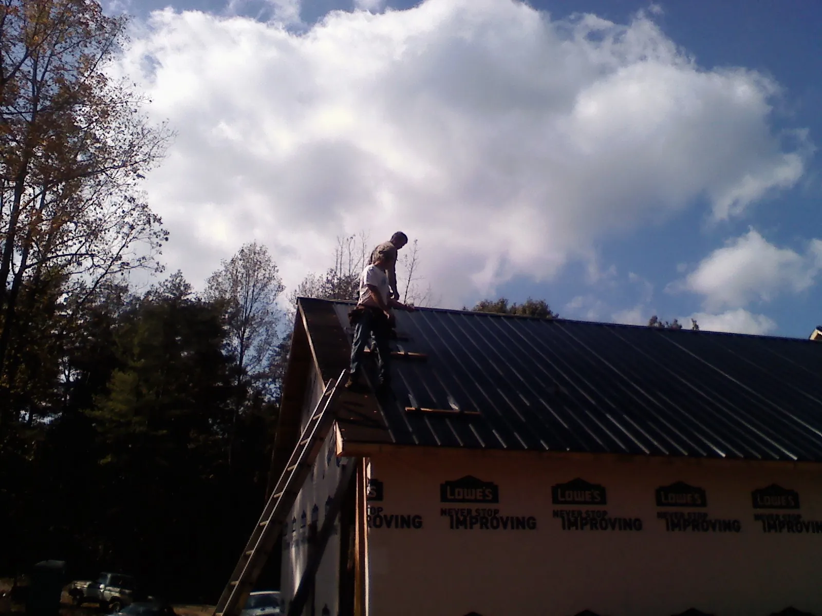Roofer fastening dark metal panels high against a cloudy sky, from a Roof Inspection job in Harwood